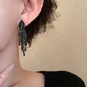 Detail von eleganten schwarzen Strass-Ohrringen mit Quasten am Ohr für einen Luxus-Look.