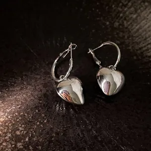 Close-up of elegant silver heart-shaped pendant hoop earrings on dark stone background