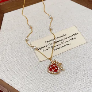 Close-up detail of a gold-plated necklace featuring a red fortune bag pendant and pearls