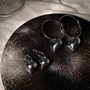 Close-up of minimalist silver heart hoop earrings in two sizes on dark ceramic plate