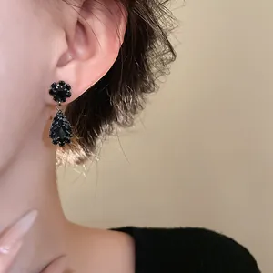 Detailaufnahme eleganter schwarzer Tropfenohrringe mit kleinen Strasssteinen an einem Model.