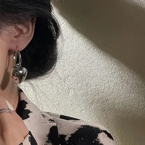 Close-up detail of a minimalist silver heart hoop earring on a model with creative shadows