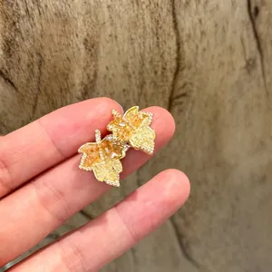 Primer plano de pendientes de botón de hoja de arce dorados con circonitas amarillas