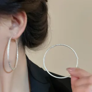 Dettaglio che mostra l'intricata trama satinata su grandi orecchini a cerchio in argento