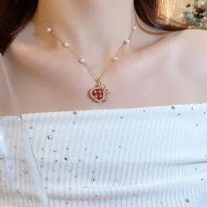 Detailed close-up of luxury gold necklace with red heart pendant and pearls worn by model.