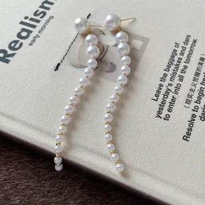 Close-up of elegant long pearl tassel earrings with gold beads on textured fabric