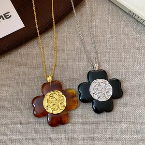 Detail of two vintage clover flower pendants in amber and black with textured metal centers.