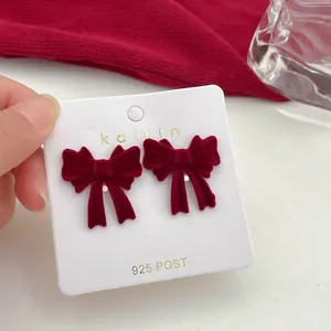 Close-up of red velvet bow stud earrings with 925 silver needles on a display card