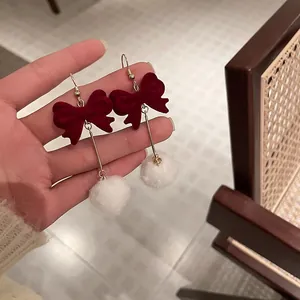 Close-up detail of vintage red velvet bow earrings with soft white pom-pom dangles