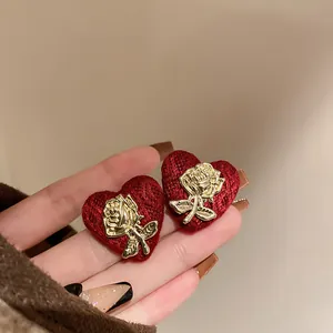 Detailed close-up of vintage red heart stud earrings with golden rose embellishment