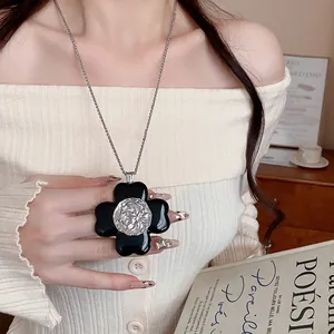 Close-up of a vintage artistic black flower pendant necklace worn over a cream knit top