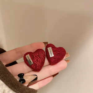 Close-up of red heart-shaped knitted stud earrings with "LOVEDAYS" metal plate detail.