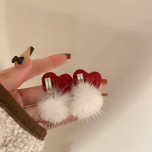 Close-up of red knit heart earrings with fluffy white pom-poms and gold metal plate