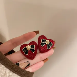 Macro detail view of vintage red knit heart earrings featuring black bow and golden flower