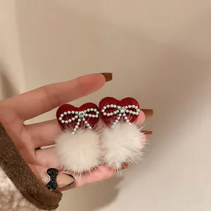 Close-up of elegant red heart earrings with pearl bows and white fluffy pom-poms.