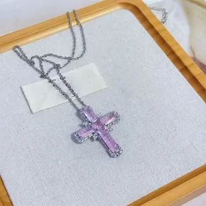 Close-up of a silver cross necklace featuring purple zircon stones on a fabric display.
