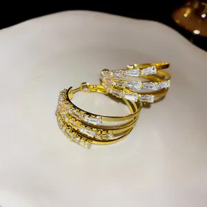 Nahaufnahme von goldfarbenen dreilagigen Creolen mit Baguette-Kristallbesatz für Damen.
