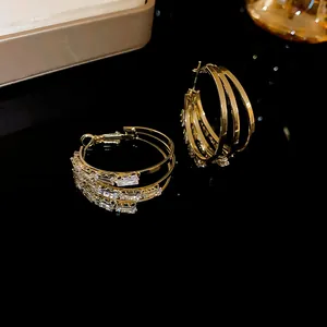 Detailansicht goldener Creolen im Dreifach-Design mit funkelnden Baguette-Kristallen