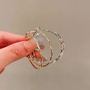 Detailed close-up of textured gold and silver hoop earrings being held by hand