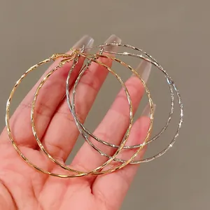Detailed view of large twisted metal hoop earrings in gold and silver finishes