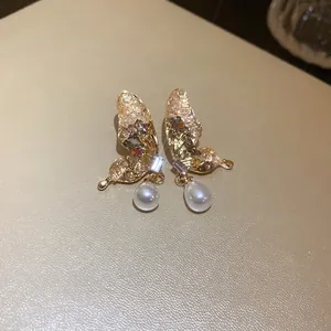 Eleganti orecchini a farfalla con cristalli e perle su superficie beige.