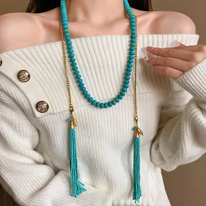 Détail d'un collier bohème en perles turquoise avec de longs glands sur un pull blanc