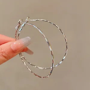 Detailed close-up view of large textured silver-tone hoop earrings being held by hand