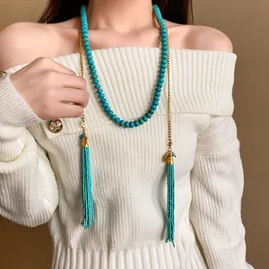 Détail d'un collier bohème avec pompons en perles porté sur un pull blanc élégant.