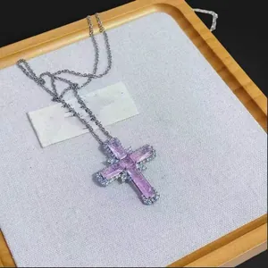 Close-up of cross pendant with purple zircon stones on a textured fabric background.