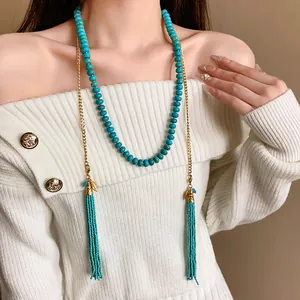 Détail du collier bohème en perles turquoise avec pompon sur un pull blanc.