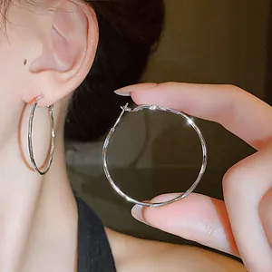 Detailed view of minimalist large twisted silver hoop earrings being worn and held.