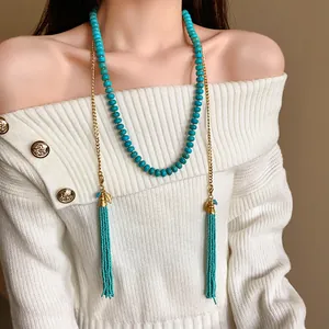 Collier bohème en perles turquoise avec de longs glands porté sur un pull blanc ajouré