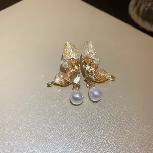 Dettaglio di eleganti orecchini a farfalla dorati con cristalli e perle a goccia.