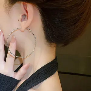 Detailed view of a large silver twisted hoop earring worn by an Asian female model