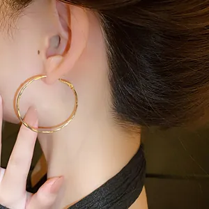 Detailed close-up of a stylish gold-plated twisted hoop earring worn by a model