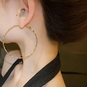 Close-up of a large twisted gold hoop earring worn by a model, showing metal texture.