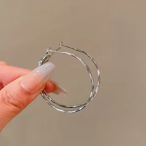 Detailed close-up view of silver-tone twisted metal hoop earrings held by hand