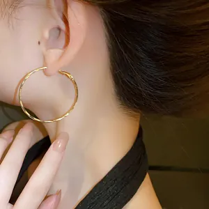 Macro detail view of elegant golden twisted hoop earrings worn by fashion model