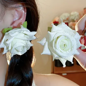 Dettagliata macro di eleganti orecchini a rosa in tessuto bianco con accenti di gocce di rugiada