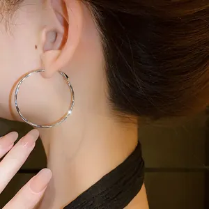 Close-up of twisted silver hoop earrings worn by a model in a minimal chic style