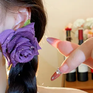 Primo piano dettagliato di un orecchino a rosa in tessuto viola con gocce di rugiada.