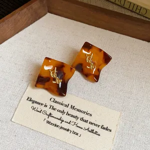 Dettaglio di orecchini quadrati in tartaruga vintage con logo dorato su vassoio.