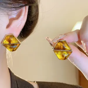 Dettaglio di orecchini geometrici color ambra con elegante montatura in metallo dorato.