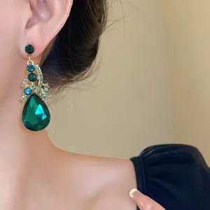 Close-up of elegant green teardrop crystal earring with gold-plated setting on model