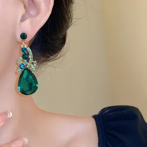 Detailed view of luxury emerald green teardrop earring with vibrant rhinestones on model