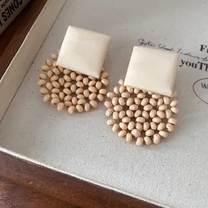 Close-up of bohemian square wood and circular beaded earrings in cream and natural tones