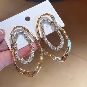 Detalle de pendientes ovalados irregulares chapados en oro con aro interior de strass.