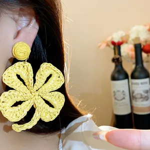Close-up of yellow raffia woven flower earring on ear, showing natural straw texture.