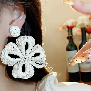 Detailed close-up of white woven raffia flower earrings in bohemian vacation style.