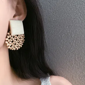 Close-up view of bohemian style square beaded earrings worn on ear with natural wooden beads